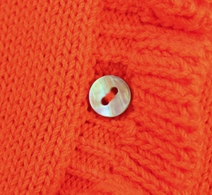 Détail macro du cardigan en maille orange avec bouton en nacre et texture tricotée