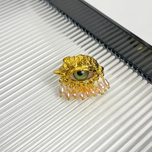 Detail of gold evil eye ring with green iris and pink teardrop pearl charms