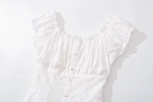 Detailed view of white short-sleeve top featuring floral embroidery and lace ruffles