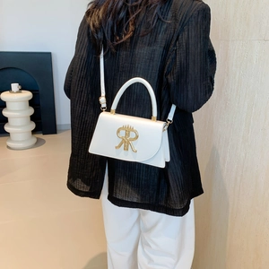 Minimalist white leather crossbody bag with gold logo on a model in a bright room