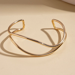 Close-up of polished golden wave double-layered open cuff bracelet with minimalist design