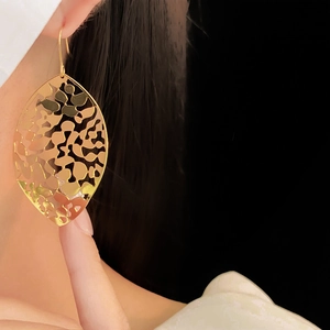 Close-up of model wearing gold hollow leaf earrings with detailed metallic vein patterns