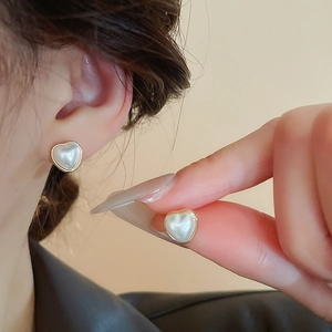 Vue détaillée des boucles d'oreilles cœur en perle avec bordure dorée sur l'oreille