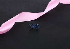 Close-up of deep blue round crystal stud earrings on black background with pink ribbon