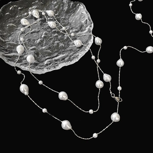Elegant irregular pearl necklace with silver chain on black background with glass saucer