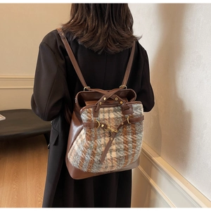 Detail view of large plaid canvas and brown leather backpack on model in a minimalist room