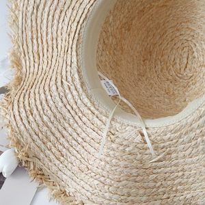 Interior detail of beige paper straw sun hat with frayed edge and 100% paper material label