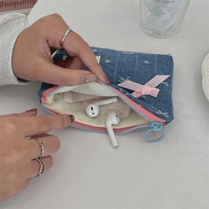 Detailed shot of denim coin purse with pink bow, holding wireless earphones inside