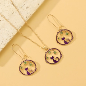 Detail of gold cat and star jewelry set featuring purple enamel pendants on stone background