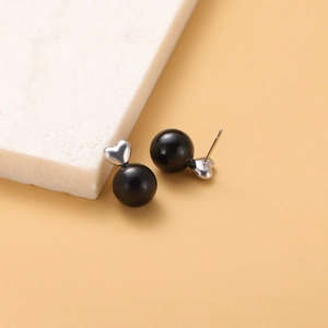 Close-up of vintage earrings featuring black pearls and silver heart-shaped studs