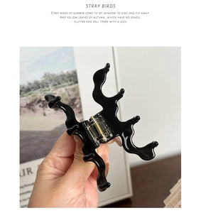 Detail of a wavy black acetate hair claw clip with a glossy finish and gold spring