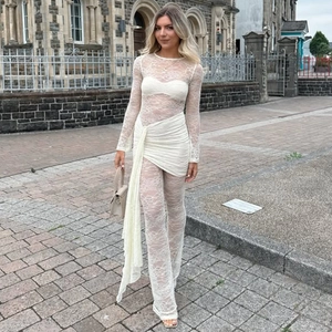 Full view of white sheer lace jumpsuit with elegant waist ruffles on a street model