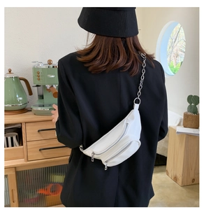 Detailed view of white faux leather chest bag with silver chain strap worn by a model