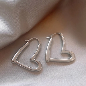 Macro shot of silver heart-shaped hoop earrings on soft champagne silk fabric