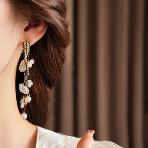 Detail of floral tassel earrings with pearls and gold chain worn by a model