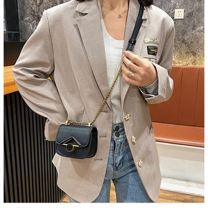 Dettaglio della mini borsa nera a tracolla con catena dorata su blazer beige