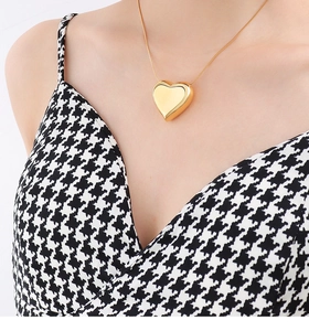 Detailed close-up of a 3D gold heart pendant necklace on a model wearing houndstooth