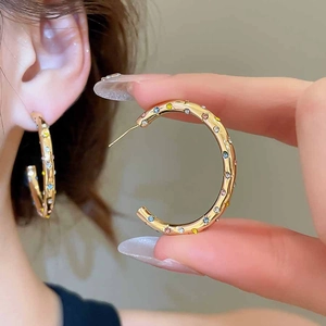 Détail de boucles d'oreilles créoles dorées en C avec strass colorés sur l'oreille