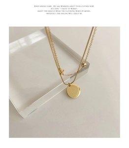 Close-up of double layer gold necklace with X charm, crystal and engraved round pendant
