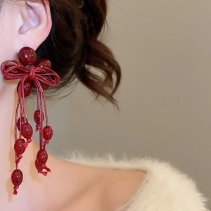 Close-up of deep red resin bead tassel earrings with hand-woven bow detail on a model