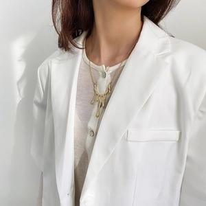 Detail of gold lava drop necklace styled with a white blazer for a minimalist look