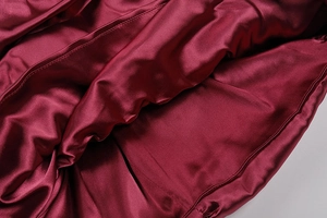 Dettaglio ravvicinato del tessuto satin rosso vino con cuciture e lucentezza seta