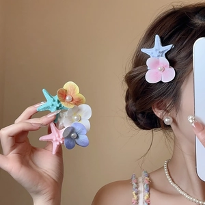 Detail of starfish and flower hair clip with pearls shown on model and held in hand