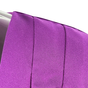 Detail of purple long-sleeved dress showing textured crepe fabric and pleated craftsmanship