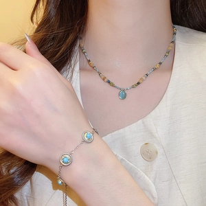 Close-up of beaded necklace with blue oval pendant and matching silver bracelet on model