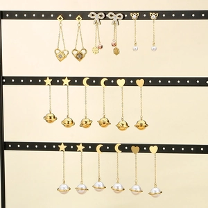 Detailed view of gold dangling earrings with pearls, hearts and star motifs on a stand