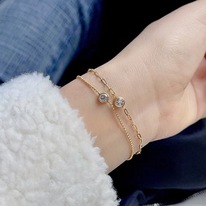 Close-up of gold paperclip and bead bracelets with round zircon worn on a cozy sweater
