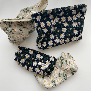 Close-up of embroidered daisy patterns on cotton canvas cosmetic bags in black and beige