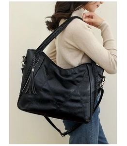 Detail of black textured leather bag with woven shoulder strap and tassel charm