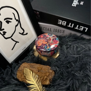 Artistic mandala patterned tin candle on grey plush rug with decorative art and books