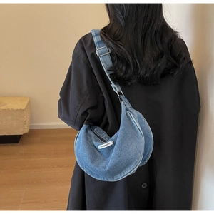 Detail of blue denim crescent bag with white fashion tag and adjustable wide strap