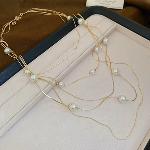 Close-up of layered faux pearl necklace with gold-tone chains on a beige jewelry display