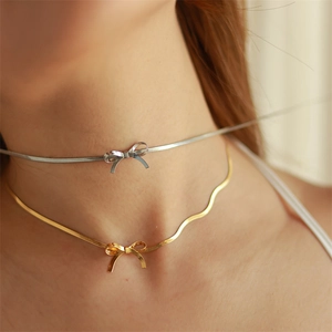 Macro shot of 18K gold and silver bow pendant necklaces on a sleek snake chain