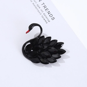 Elegant black crystal swan brooch with faceted gemstones and red beak on a white surface