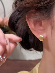 Detail of 18k gold plated oval earrings with brushed metal texture on female model