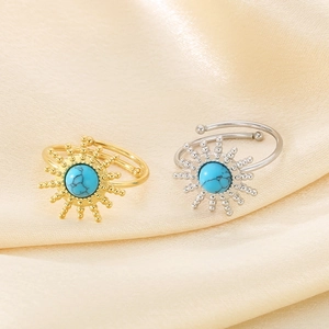 Detailed close-up of gold and silver sunflower rings with blue turquoise on satin fabric