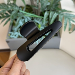 Dettaglio della grande pinza per capelli nera opaca con design traforato tenuta in mano