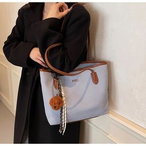Detail of light blue canvas tote bag with brown leather handles and teddy dog charm