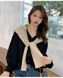 Detail view of model wearing a beige knitted hooded scarf shawl over a black shirt