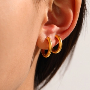Macro side view of elegant matte gold brushed hoop earrings on a female model's ear