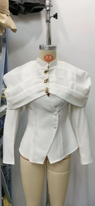 Detail of white blazer featuring sculptural pleats and gold teardrop buttons