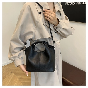 Detail of black pebbled leather bucket bag styled with a beige trench coat on a model