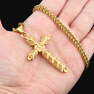 Détail d'un pendentif croix ornée dorée avec gravures de vigne sur une chaîne en épi