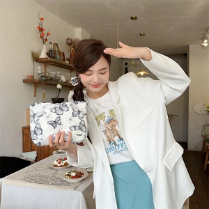 Close-up of a stylish white lace pouch with black butterfly patterns in a cafe setting