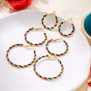 Detailed view of three pairs of red and green enamel twisted hoop earrings on ceramic tray