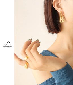 Close-up of gold stainless steel letter B earrings and textured ring on a fashion model
